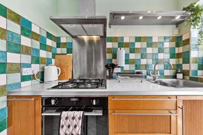 A kitchen with a gas stove, stainless steel range hood, wooden cabinets, and a tiled backsplash. - Dartford Dream House Retreat (Dartford)
