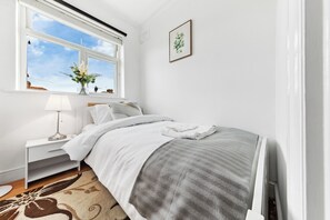 Ein Schlafzimmer mit Bett, Nachttisch, Lampe, Fenster mit Aussicht und einem gerahmten Bild an der Wand.