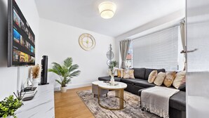 A modern living room with a flat-screen TV, a sofa, a coffee table, and a decorative wall clock. - Cozy 3bd, Garden, Free Parking, M25,Bluewater (Dartford)