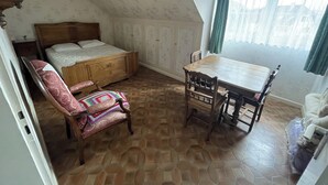 A bedroom with a wooden bed, a wooden chair, a wooden table, and a window with curtains.