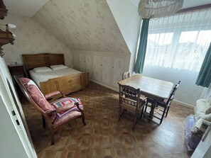 A bedroom with a wooden bed, a wooden chair, a wooden table, and a window with curtains.