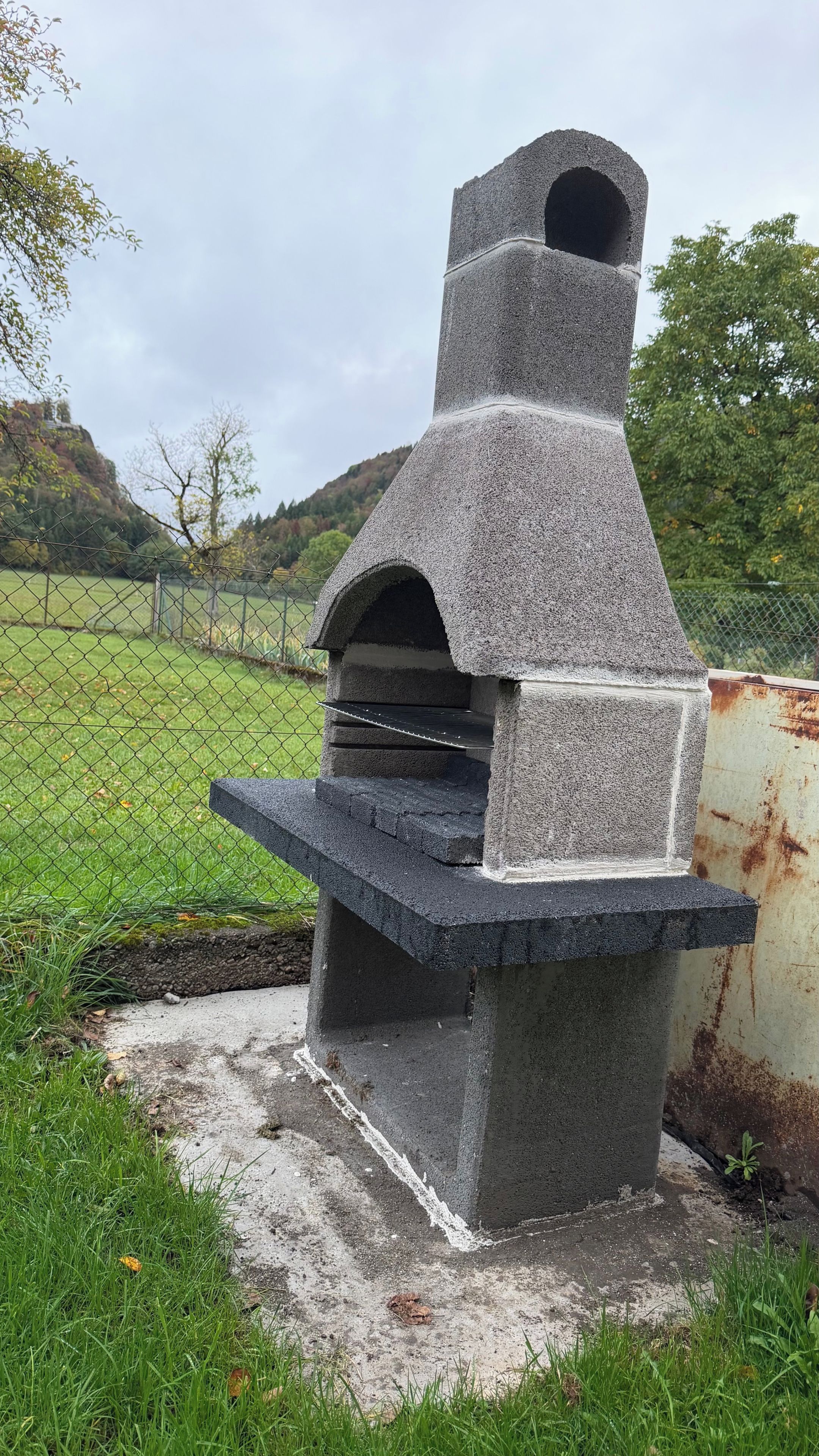 Een bakoven van natuursteen, met schoorsteen, omringd door een grasveld en een hek.