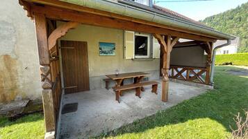 Eine Holz-Pergola mit Picknicktisch, Bänken, einer Tür und einem Fenster mit Fensterläden.
