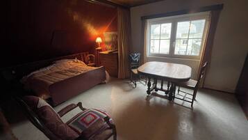 Une chambre à coucher avec un lit, une table en bois, une chaise, une lampe et une fenêtre.