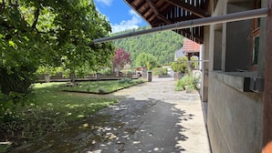 A pathway leading to a building with a wooden roof, surrounded by greenery and a clear sky.