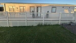 Une maison mobile de plain-pied avec un jardin avant clôturé, une véranda et un petit espace jardin.