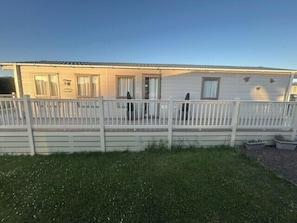 Une maison mobile de plain-pied avec un jardin avant clôturé, une véranda et un petit espace jardin.