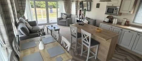 Un amplio espacio habitable con un conjunto de sofás, una mesa de comedor con sillas, una cocina con microondas y un gran ventanal.
