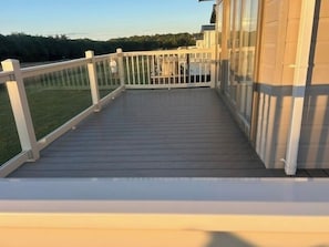 Une terrasse en bois avec une balustrade blanche, une porte vitrée et une vue sur un espace verdoyant.