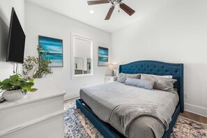 Ein Schlafzimmer mit einem Bett, einem Deckenventilator, einem Fernseher und Kunstwerken an den Wänden.