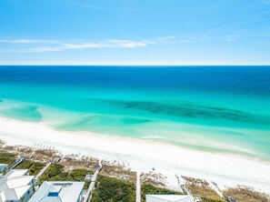 Blick auf die Küste mit Strand, klarem, blauem Wasser und einem Weg zu einem Gebäude mit blauem Dach.