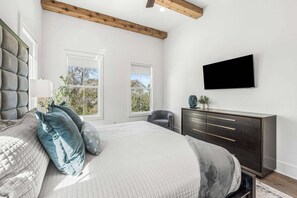 Ein Schlafzimmer mit einem Bett, einem Schminktisch, einem Sessel und einem an der Wand befestigten Fernseher.
