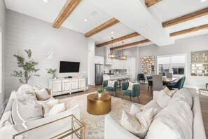 A spacious living room with a large sofa, a coffee table, and a television. There is a kitchen area with modern appliances and a dining space with chairs. - Sleeps 20! LSV/Golf Cart, Bikes & Private POOL! Pet-Friendly! (Santa Rosa Beach)