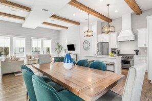 A modern kitchen with white cabinetry, a central island, and a dining area with a wooden table and teal chairs. - Sleeps 20! LSV/Golf Cart, Bikes & Private POOL! Pet-Friendly! (Santa Rosa Beach)