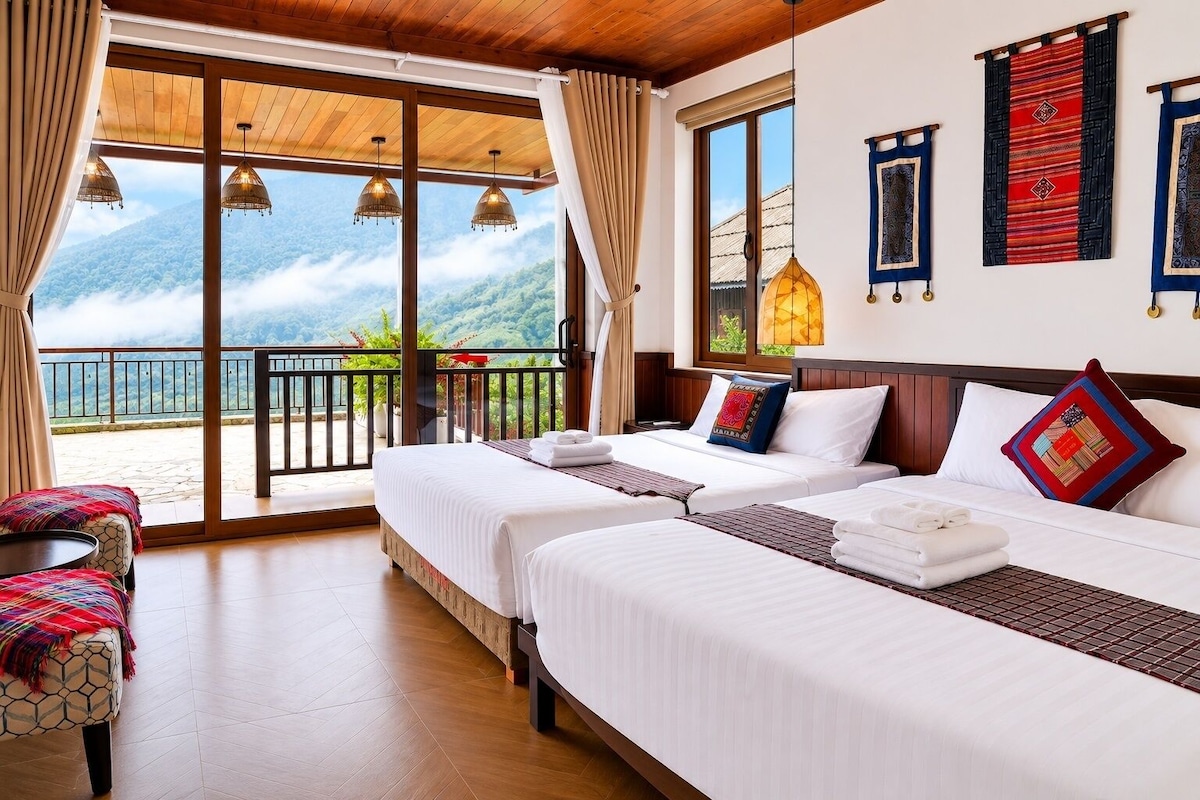 A hotel room with two beds, a balcony with a view of the mountains, and a dining area.