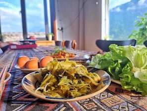 A dining table with a plate of cooked greens, eggs, and a bowl of salad, set on a patterned tablecloth. - Larosa Homestay Sapa (Ta Van)
