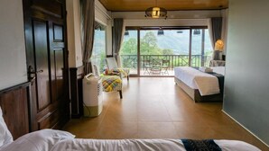 Habitación de hotel con cama, una silla, una mesa y un balcón con vistas a las montañas.