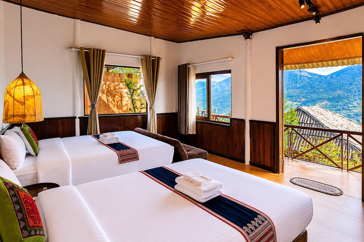 A hotel room with two beds, a wooden ceiling, a view of mountains, and a balcony.