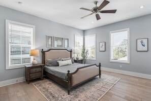 A bedroom with a bed, nightstand, lamp, ceiling fan, and framed artwork on the walls. - Sleeps 30! LSV/Golf Cart, Private Pool, HotTub, & Game Room! Pet-Friendly (Santa Rosa Beach)