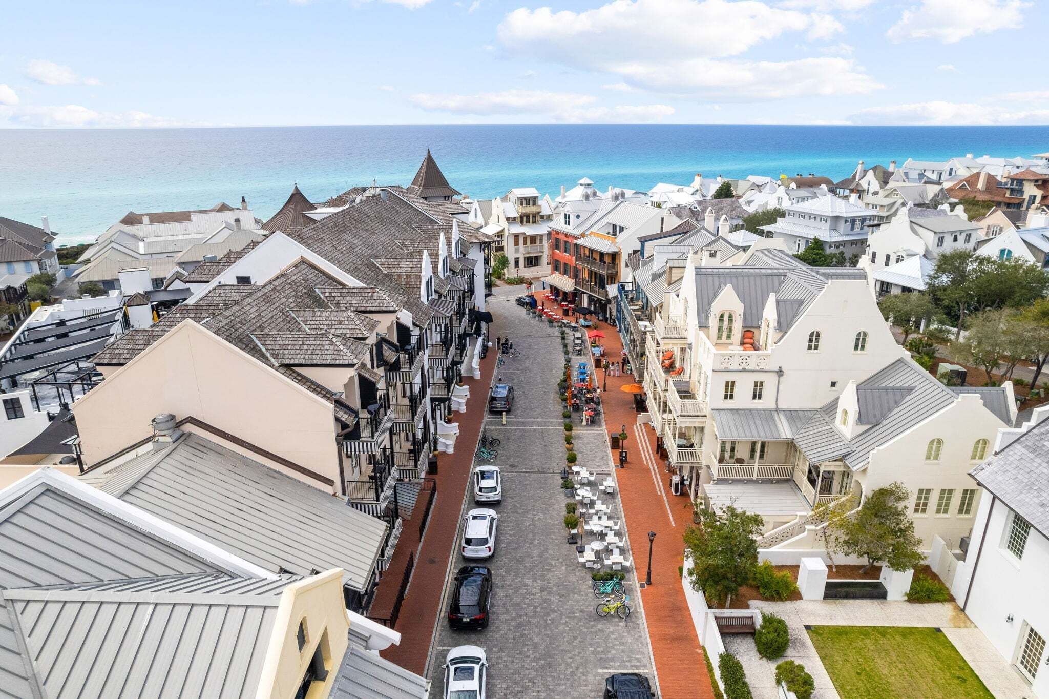 A coastal town with a narrow street lined with buildings, a clear view of the sea, and parked cars.