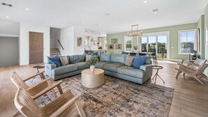 A spacious living room with a large L-shaped sectional sofa, a round coffee table, and wooden chairs. - Sleeps 30! LSV/Golf Cart, Private Pool, HotTub, & Game Room! Pet-Friendly (Santa Rosa Beach)