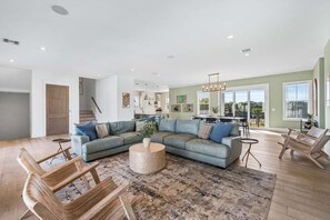 A spacious living room with a large L-shaped sectional sofa, a round coffee table, and wooden chairs. - Sleeps 30! LSV/Golf Cart, Private Pool, HotTub, & Game Room! Pet-Friendly (Santa Rosa Beach)