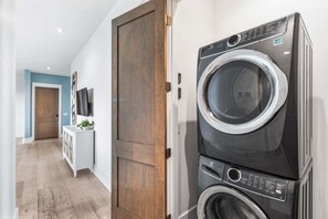 A laundry room with stacked washers and dryers, a wooden door, a white cabinet, and a television on the wall. - Sleeps 30! LSV/Golf Cart, Private Pool, HotTub, & Game Room! Pet-Friendly (Santa Rosa Beach)