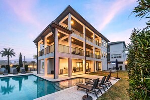 A multi-story building with a pool, outdoor seating, and a well-lit patio area. - Sleeps 30! LSV/Golf Cart, Private Pool, HotTub, & Game Room! Pet-Friendly (Santa Rosa Beach)
