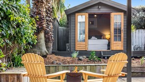 A small cabin with an open bedroom door, a fire pit, and two Adirondack chairs in the foreground. - Pomora Family Escape Close to Beach & Golf (Torquay)