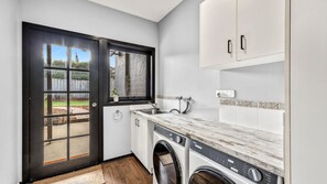 A compact laundry room with a washing machine, a sink, and a window overlooking a backyard. - Pomora Family Escape Close to Beach & Golf (Torquay)