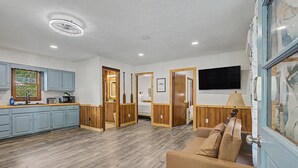 Una habitación amplia con suelo de madera, un sofá, televisión y una zona de cocina con armarios y ventana.