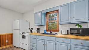Una cocina con electrodomésticos blancos, armarios azules, una encimera de madera y una ventana con vistas.