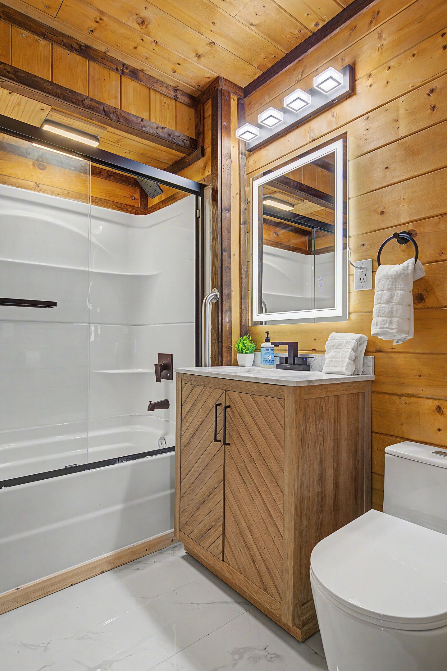 A wooden-paneled bathroom with a glass shower enclosure, a vanity with a mirror, and a toilet.