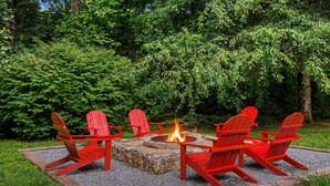 Un hogar de fuego rodeado por cuatro sillas Adirondack rojas en un jardín.