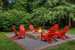 Een vuurkorf omringd door vier rode Adirondack-stoelen in een tuin.