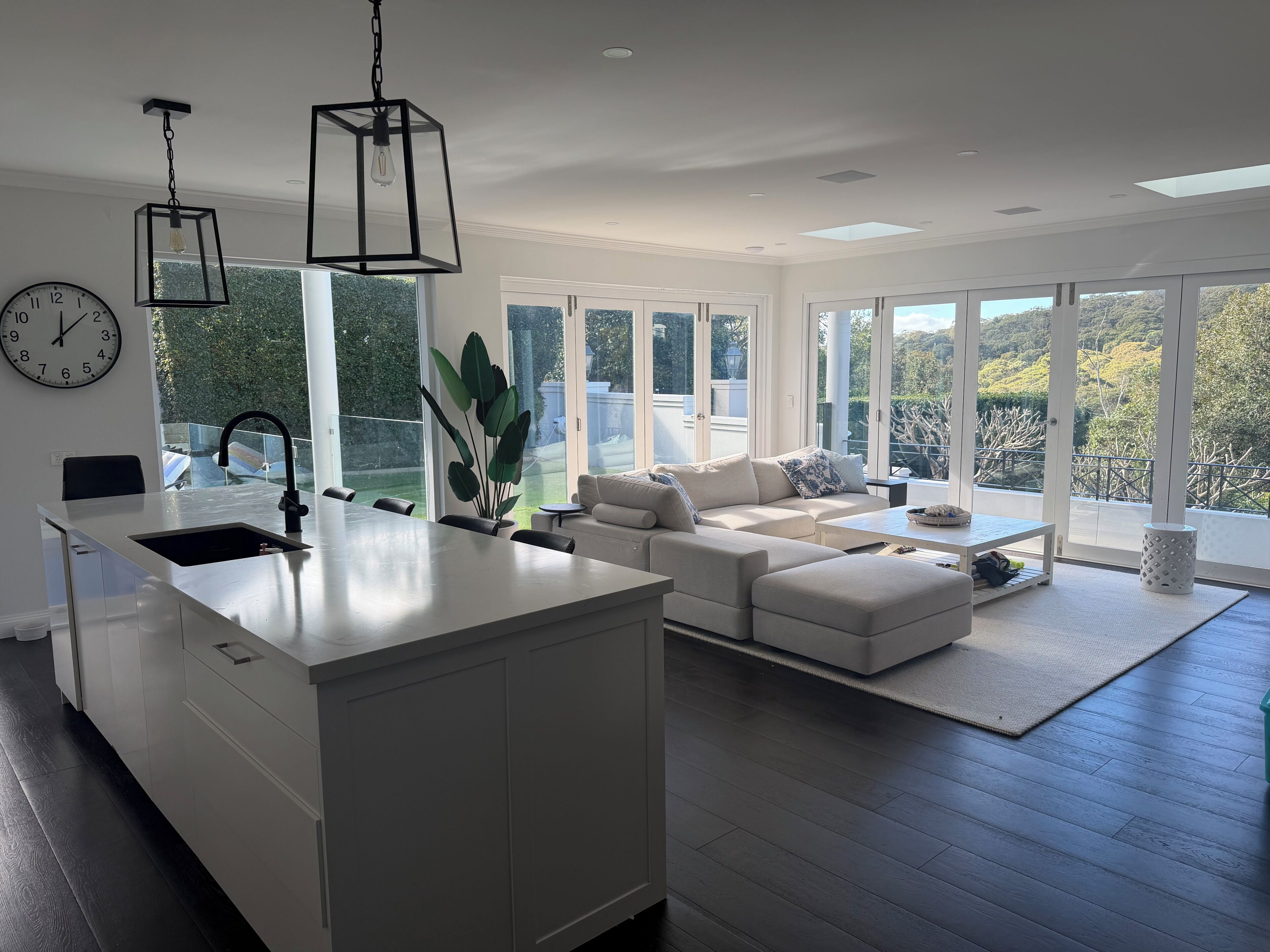 A modern kitchen with a central island, a dining area with a sofa, and large windows offering a view of the outdoors.