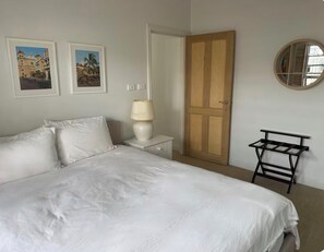 Ein Schlafzimmer mit einem Bett, einem Nachttisch, einer Lampe, einer Holztür, einem an der Wand befestigten Spiegel und zwei gerahmten Bildern.
