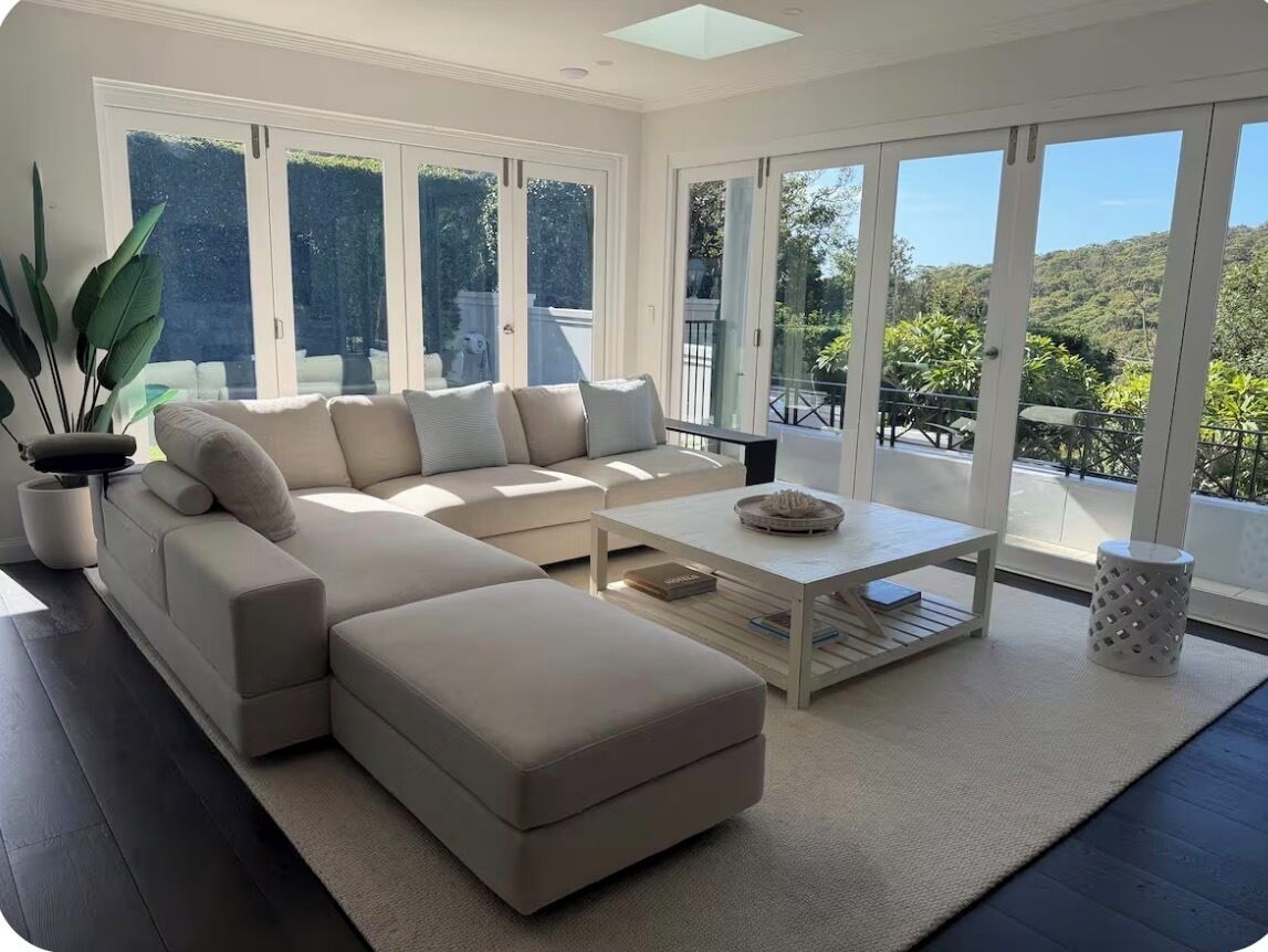 A modern living room with a sectional sofa, a coffee table, and large windows offering a view of greenery.