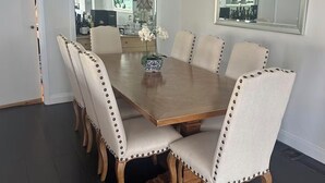 Uma sala de jantar com uma mesa de madeira retangular cercada por seis cadeiras estofadas com costura decorativa.