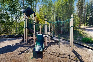Ein Spielplatz mit Rutsche, Klettergerüsten und einer Seilnetzbrücke.