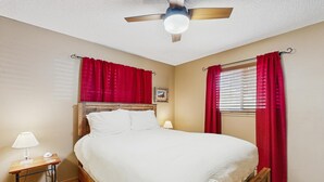 A bedroom with a wooden bed, red curtains, a ceiling fan, and a bedside table with a lamp. - Conveniently located condo w/ fast wifi, great location & shared pool & hot tub (Winter Park)