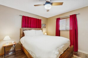 Ein Schlafzimmer mit einem hölzernen Bett, roten Vorhängen, einem Deckenventilator und einem Nachttisch mit Lampe.
