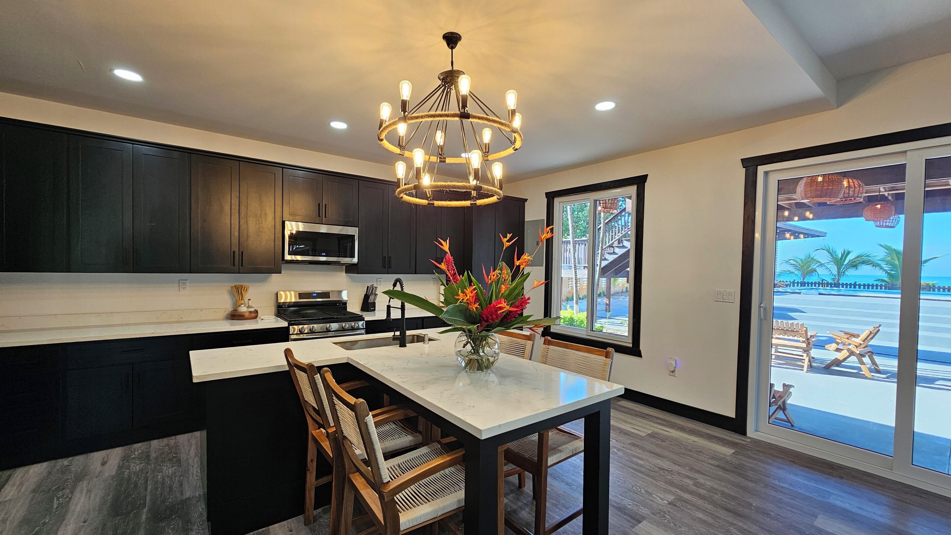 A modern kitchen with dark cabinets, a stainless steel microwave, and a large island with chairs.