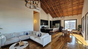 A modern living room with a sectional sofa, a dining area with a table and chairs, a kitchen with dark cabinets, and a wooden ceiling. - Casa Buenas Vibras 5-bedroom Beach Front house in Rio Maria (Rio Maria)