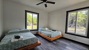 Un dormitorio con dos camas, ventanas amplias, ventilador de techo y vista a un jardín.