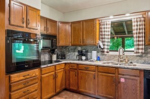 A kitchen with wooden cabinets, a microwave, a coffee maker, and a window with curtains. - New! Dollywood~Secluded~Hot Tub~King Suite~Firepit (Sevierville)