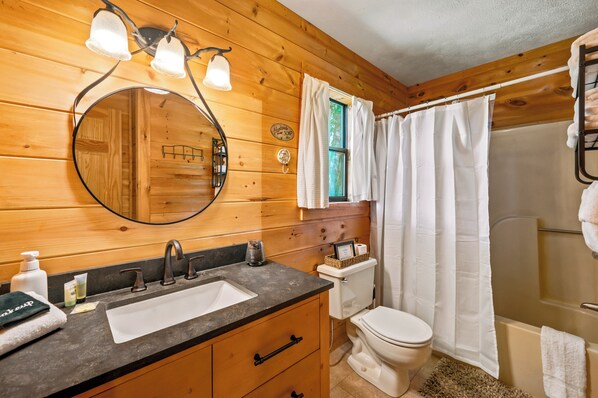 A wooden cabin bathroom with a sink, mirror, toilet, and shower. - New! Dollywood~Secluded~Hot Tub~King Suite~Firepit (Sevierville)