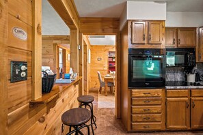 Un intérieur en bois comprenant un espace cuisine équipé d’un four et d’un micro-ondes Whirlpool, de meubles de rangement en bois et d’un coin bar avec des tabourets.