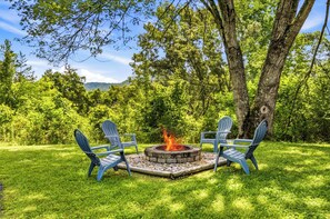 A fire pit with two Adirondack chairs in a grassy area surrounded by trees. - New! Dollywood~Secluded~Hot Tub~King Suite~Firepit (Sevierville)