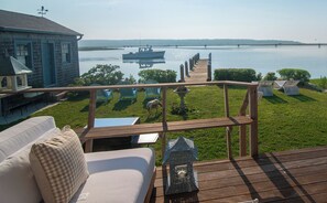A deck with a view of a calm lake, a boat, and a distant bridge.